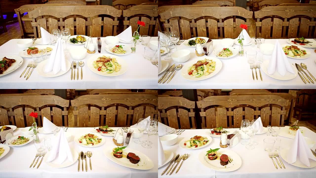 餐厅的宴会桌，餐桌上的饭菜，叉子眼镜，刀子，餐具躺在盘子旁，食物放在漂亮的白色桌子上