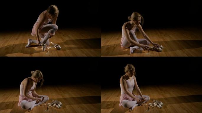 金发芭蕾舞女演员解开鞋子，坐在地板上累了