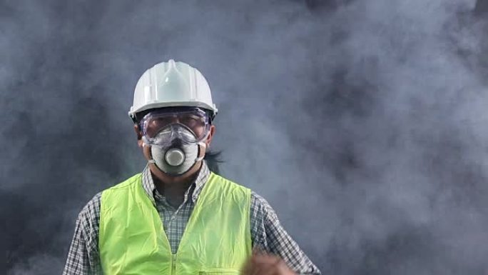 肖像亚洲工人穿着安全防护装备、护目镜、面具、帽子、背心在危险烟雾黑暗的房间里