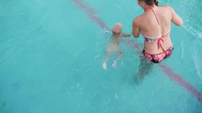 一岁的小女孩牵着妈妈的手跳进游泳池