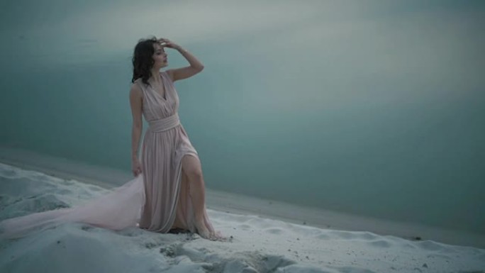 年轻的幻想女孩站在湖岸的沙丘上。漂亮无辜的仙女在晚上放松