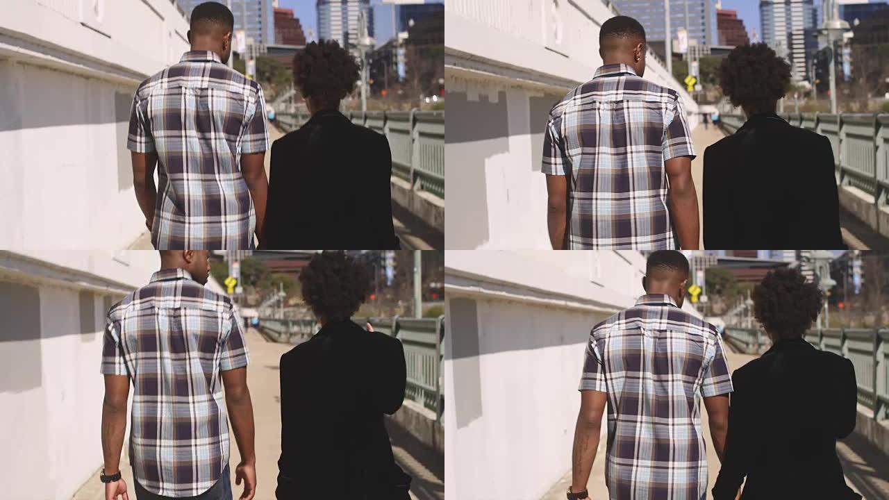 非洲裔美国夫妇牵着手走在人行道上，从后面看