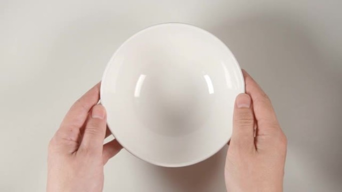 俯视图: 人类的手将一个白色的汤碗放在白色的桌子上