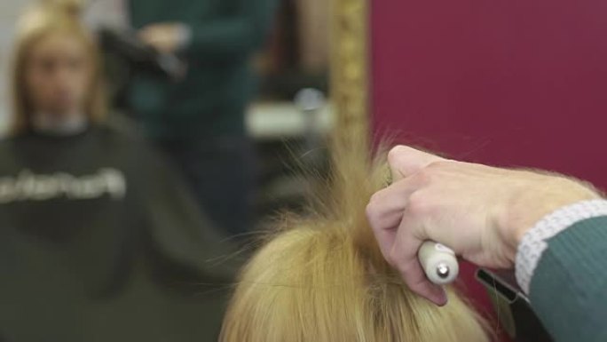 理发师风格的头发顶部到金发女孩的梳子和吹风机在美容沙龙。制作体积
