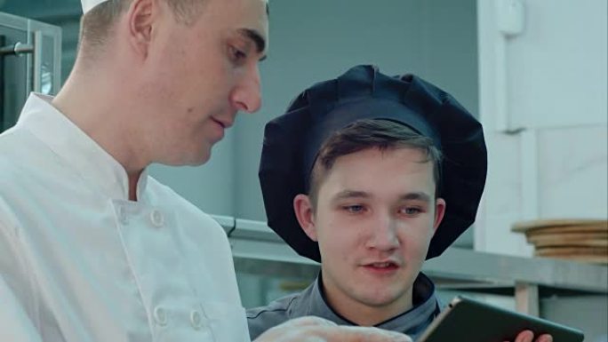 主厨使用数字平板电脑向帽子里的厨师讲解一些东西