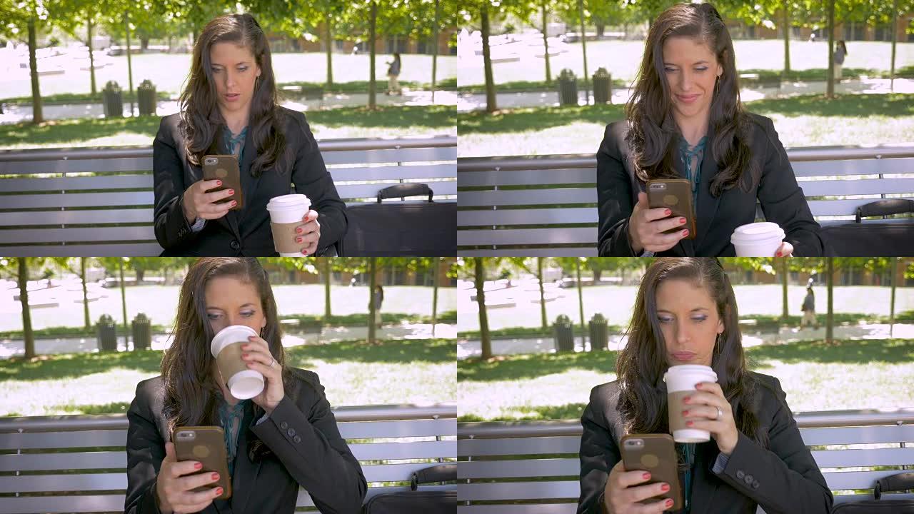 女人坐在公园的长椅上，微笑着喝着智能手机上的咖啡