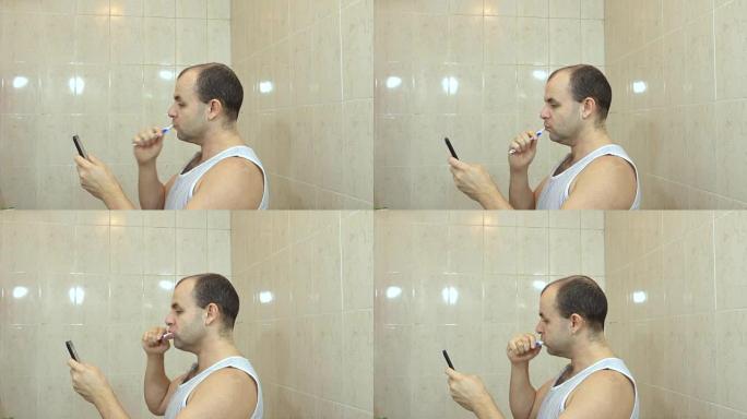 肖像成年男子在家庭浴室刷牙，拿着牙刷和使用智能手机。