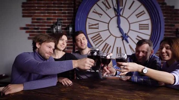 五个老朋友在餐厅庆祝周年纪念日，并互相喝红酒，高兴地碰杯。人们坐在桌旁，一边一起敬酒一边擦着酒杯