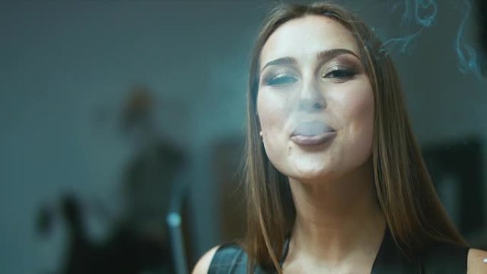 性感诱人的女人，棕色头发，从雪茄中吹入烟雾，然后吹出一个热吻