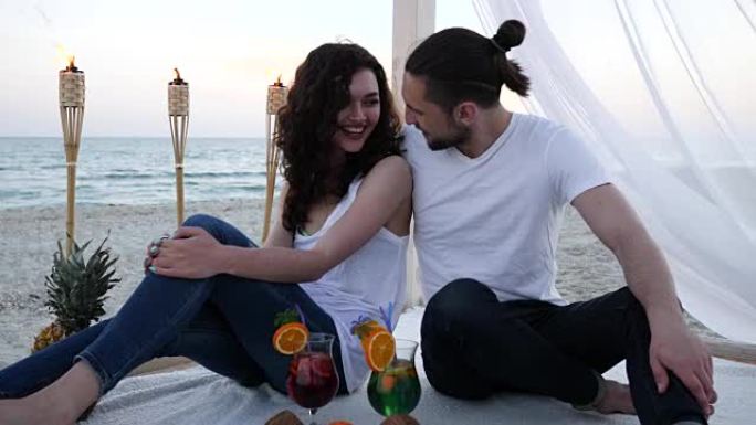 浪漫的情侣配鸡尾酒在海滩平房玩得开心异国情调的假期，背景热带水果，燃烧的火把