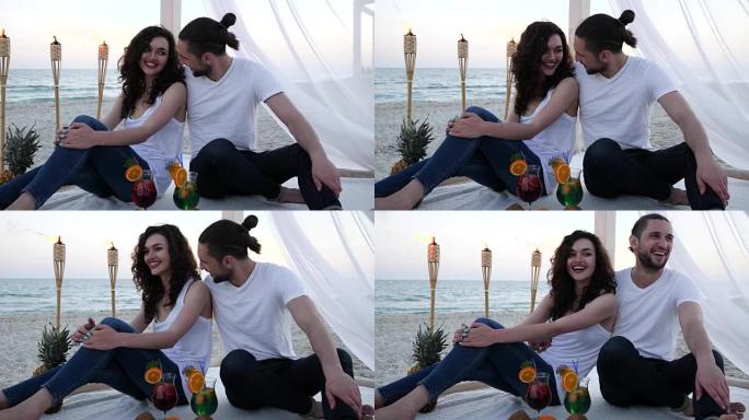 浪漫的情侣配鸡尾酒在海滩平房玩得开心异国情调的假期，背景热带水果，燃烧的火把