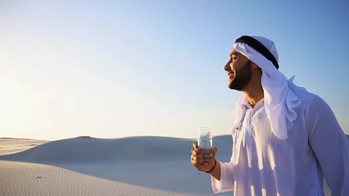 在沙质沙漠干燥的气候中，男性穆斯林的清新气息。guy Arab在晚上露天从玻璃中喝水