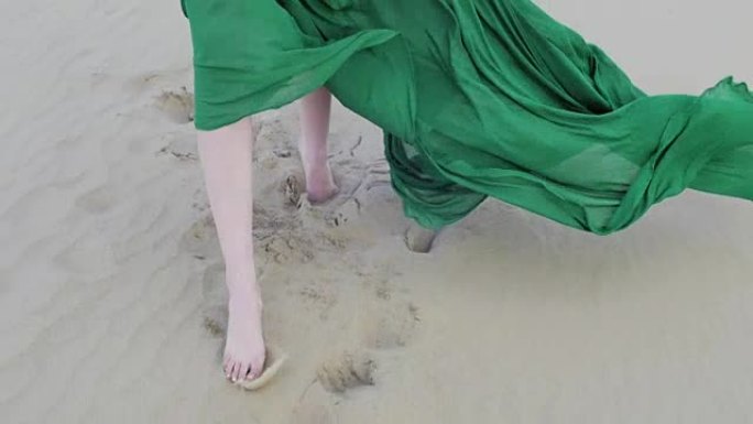 穿着绿色连衣裙的美女在沙丘上奔跑，风吹着她的衣服慢动作前视脚特写