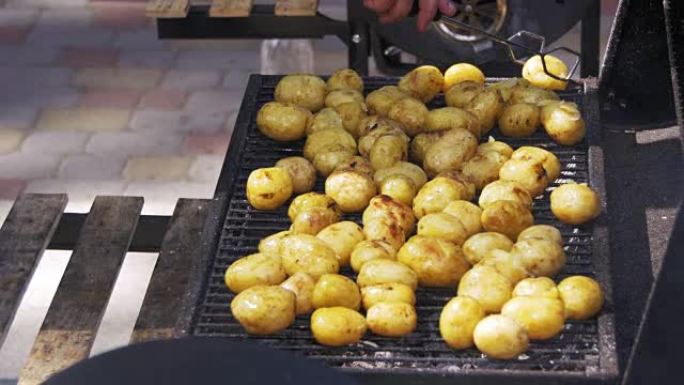 年轻的土豆在烤架上准备。用手用钳子在烤肉上转土豆