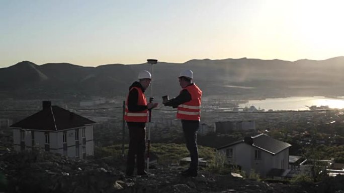 两名戴着头盔的测量员在山顶上进行测地测量