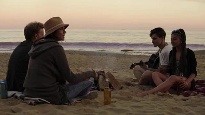 小伙伴们晚上坐在海边的火炉旁，喝着啤酒，弹着吉他。4k拍摄