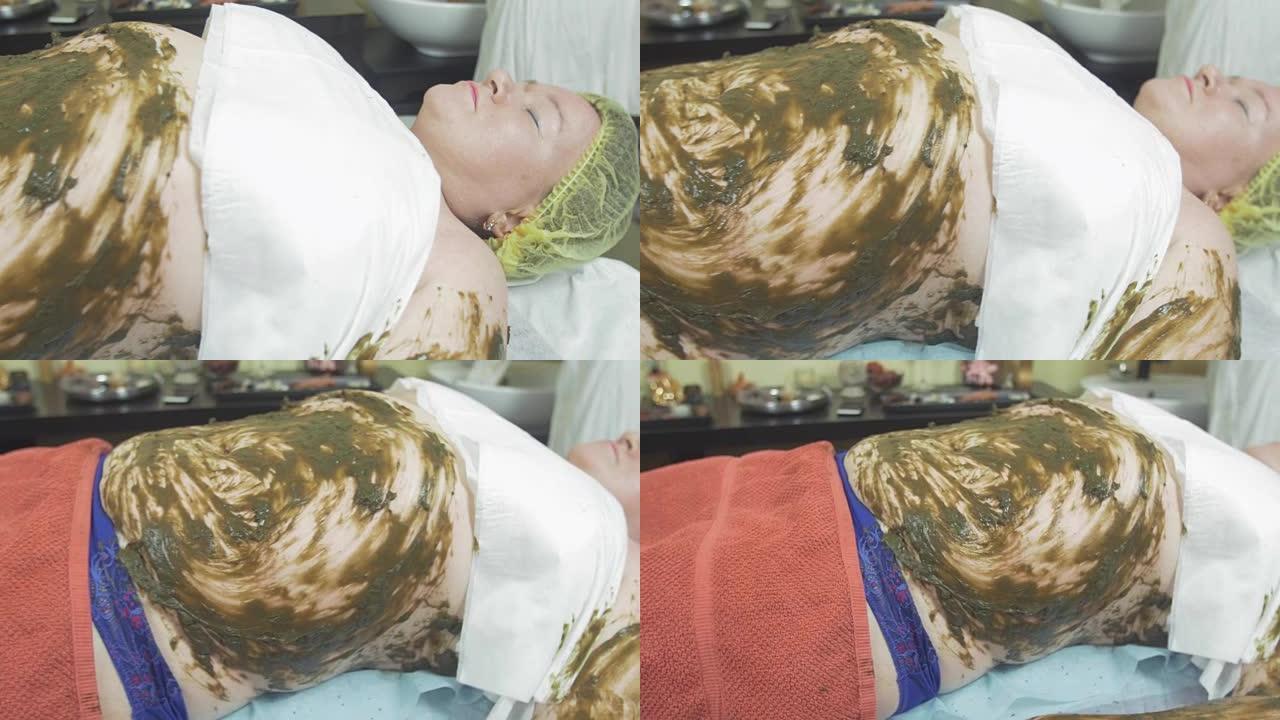 成年胖女人躺在肚子上，左手躺在海藻混合物中。水疗包装