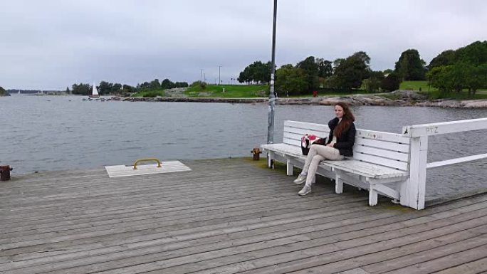 年轻女子独自坐在空荡荡的渡轮着陆台上，欣赏寒冷的灰色大海