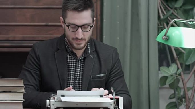 戴着眼镜的年轻作家揉搓双手，开始在红色老式打字机上打字