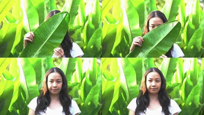 亚洲女人把表情藏在热带树叶后面。秘密揭示概念