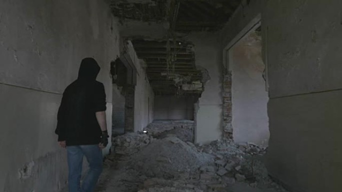 蒙面的年轻人走过一栋废弃建筑的走廊