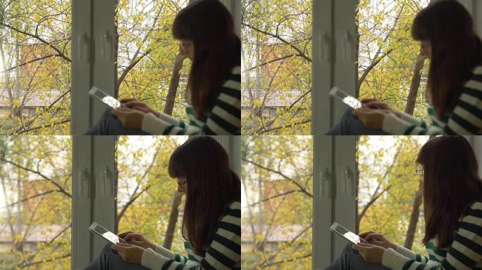 女孩坐在街上的窗台上黄叶，在网上看书。