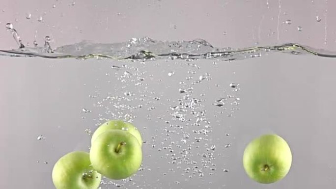 四个青苹果在灰色背景下落水，超级慢动作