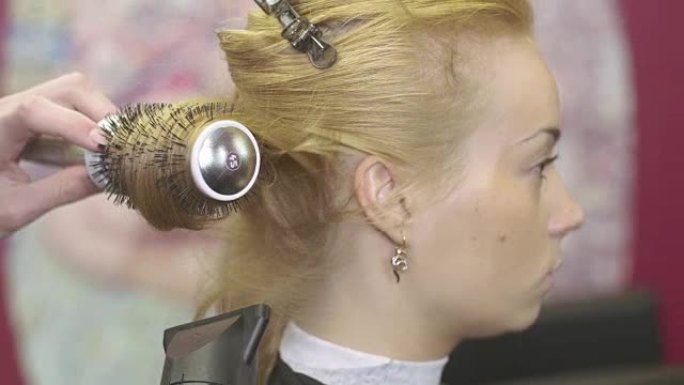 理发师在美容沙龙用梳子和吹风机拉金发女孩的头发。制作体积发型