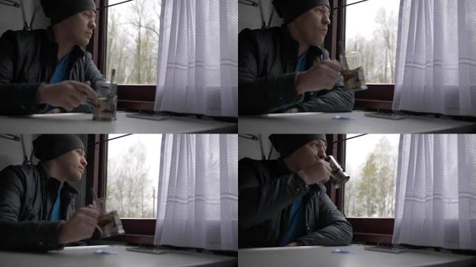 一个年轻人穿着灰色的帽子和灰色的夹克去火车上，坐在一张小桌子上，把窗帘推开窗户，偷看茶，看着窗外。窗