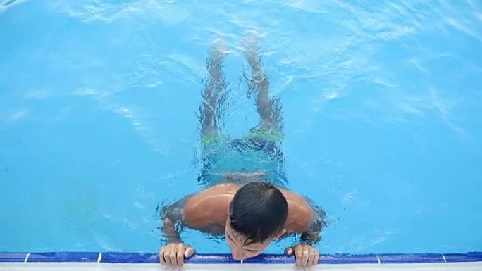 年轻人保持游泳池的边缘在水中，享受他在slo-mo的生活