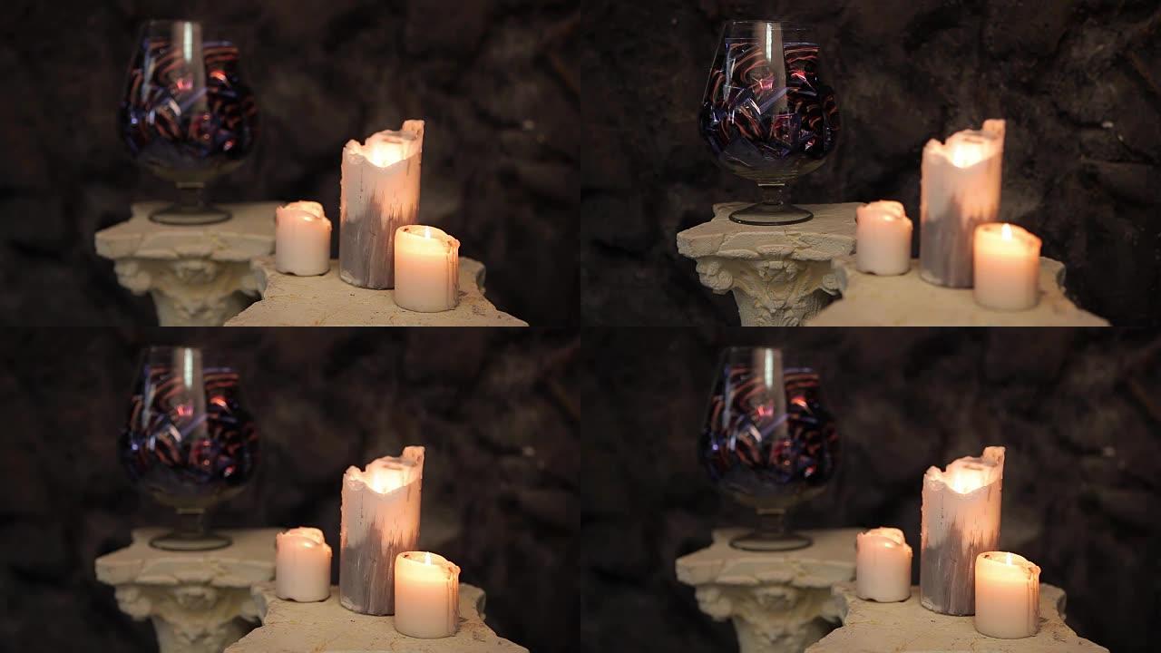 玻璃花瓶，巧克力，糖果和燃烧的蜡烛在前景。花瓶里的巧克力糖果和燃烧的蜡烛。花瓶里的巧克力糖果和糖果。