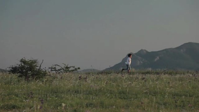 一个拿着手帕的男孩在群山的背景下跑着