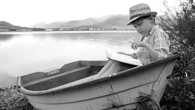 黑白画面:一个男孩坐在木船上看书
