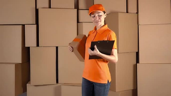 穿着橙色制服的苗条女孩在纸箱堆的背面运送包裹。全高清工作室视频