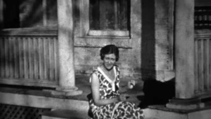 1934: 女人在前弯腰的门廊上玩黑狗。