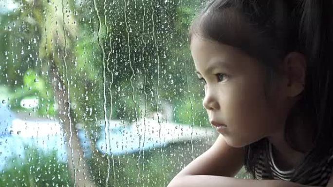 亚洲小女孩看着窗户里的雨，慢动作。