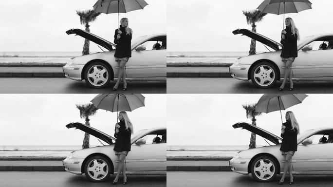 一名妇女站在破损汽车附近的雨伞下的黑白镜头