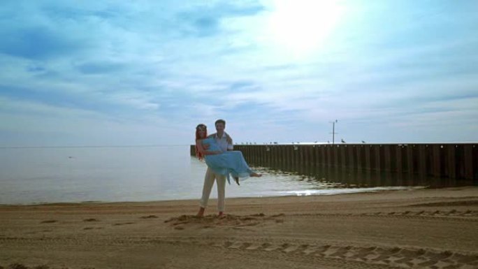 男人抱着妻子在海边。丈夫抱着怀孕的妻子