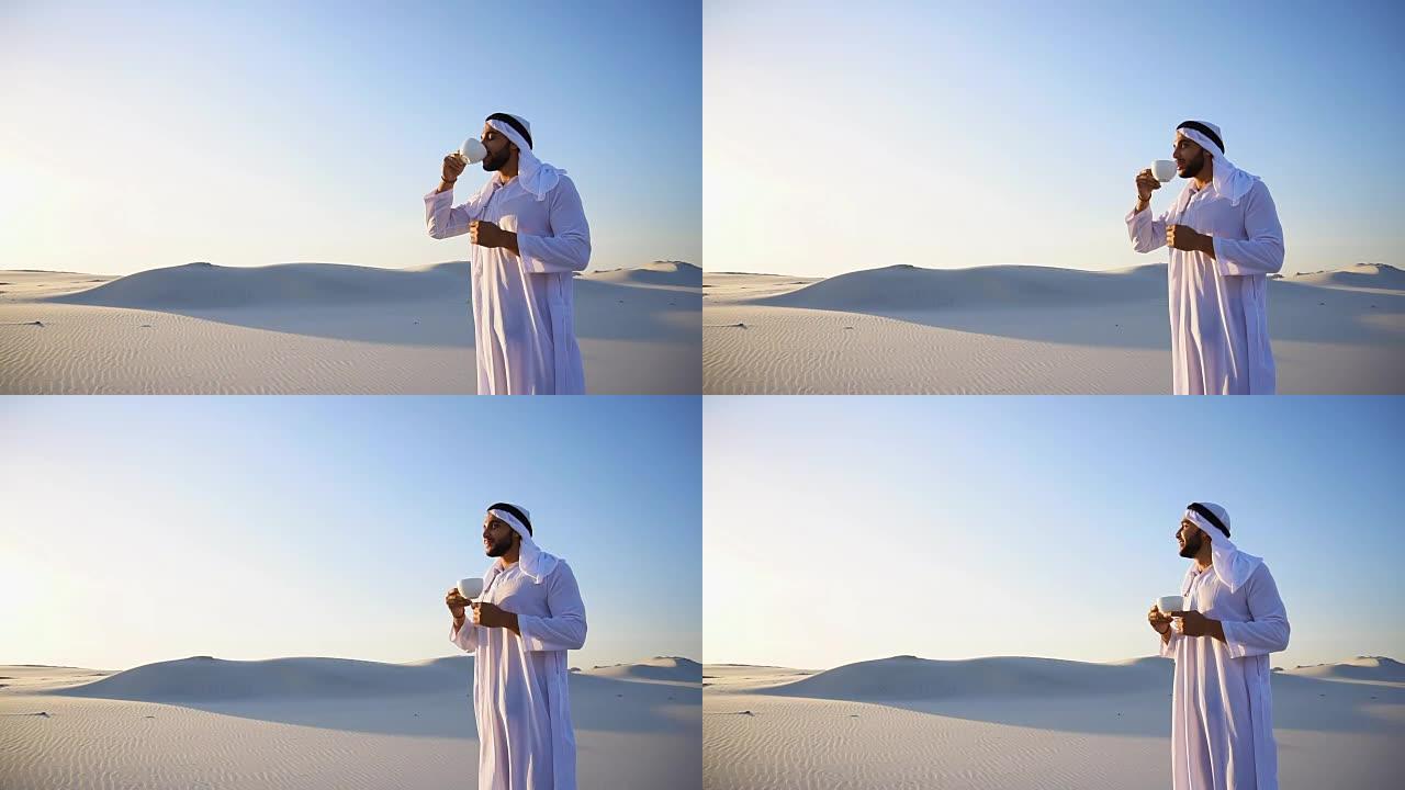 早上好，在蓝天和沙丘的映衬下，在巨大的沙漠中喝咖啡的男性酋长