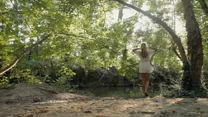 美丽的金发女郎穿着裙子在森林的池塘边休息