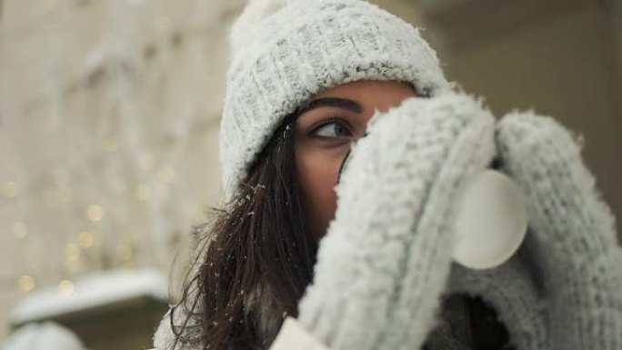 幸福，寒假，圣诞节，饮料和人们的概念-微笑的年轻女子穿着白色暖和的衣服与喝咖啡带走了雪城背景