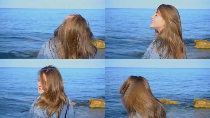 慢动作快乐的年轻女性在镜头前长出头发并摆姿势，在晴朗的早晨站在海边，在晴朗的天空背景下