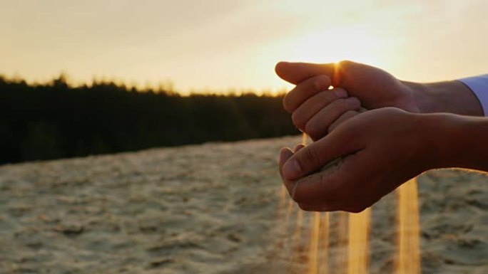 年轻人的手用手指筛沙子。当前符号时间和变化
