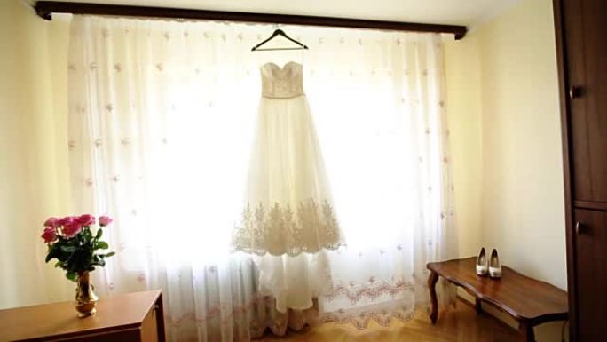 收起衣架上的时尚婚纱，地板上的白鞋和新娘房间里的粉红色玫瑰花束。