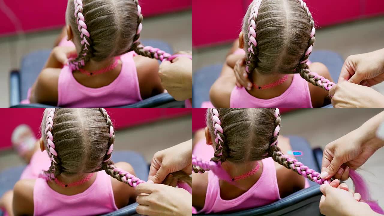 美丽的金发女孩，七岁，编织两根辫子，在一家美容院，一家理发店，在一面大镜子前，用粉红色的头发做发型。