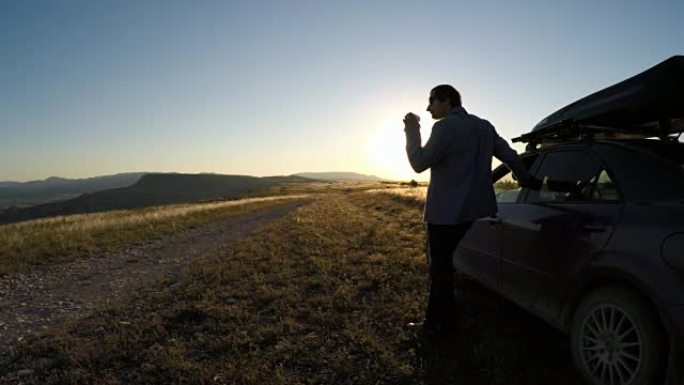 男人走近车，喝着咖啡，看着夕阳