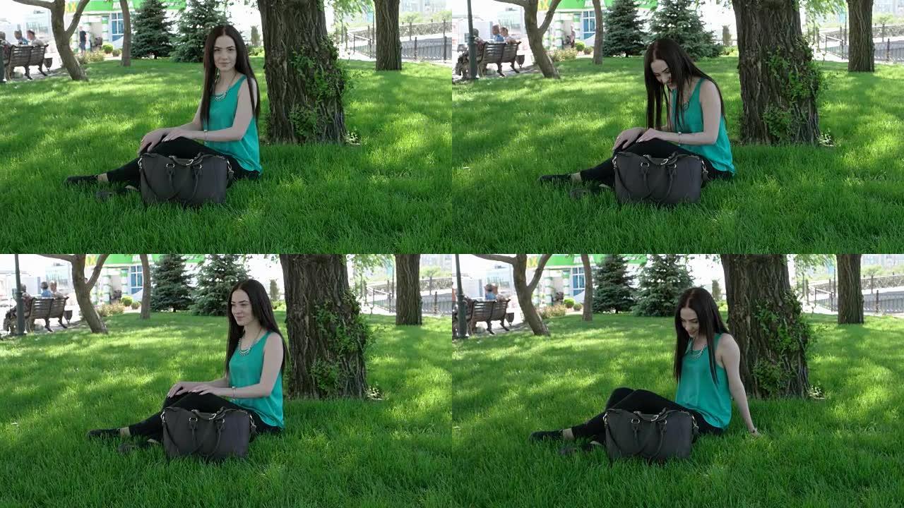 十几岁的女人坐在绿色的草地上，拿着时尚的手提包，看着相机