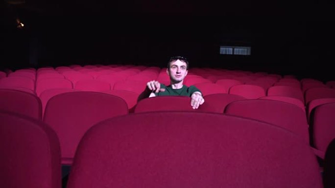 一个坐在黑暗电影院舒适的红色椅子上的男人看起来喜剧和笑声
