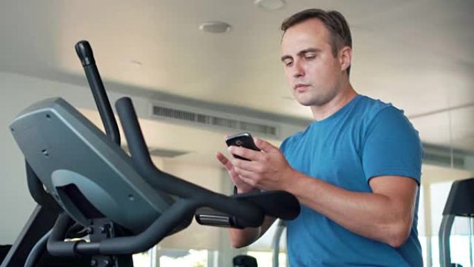 英俊健康的年轻人在健身房锻炼。使用智能手机，与朋友进行消息传递