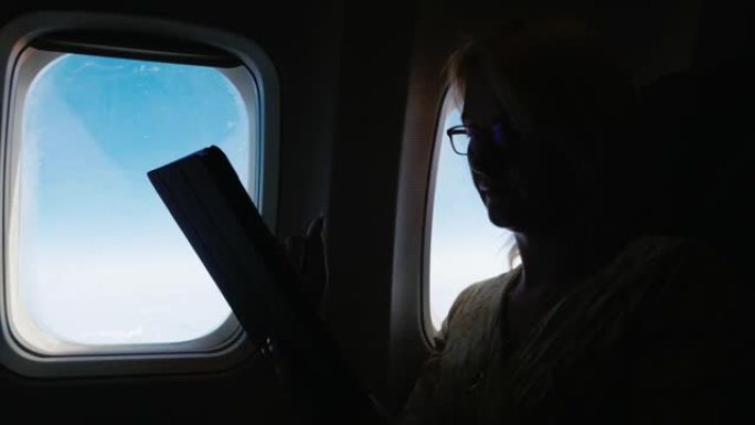 一个女人正在乘飞机飞行，在平板电脑上阅读一些东西。侧影，侧视图